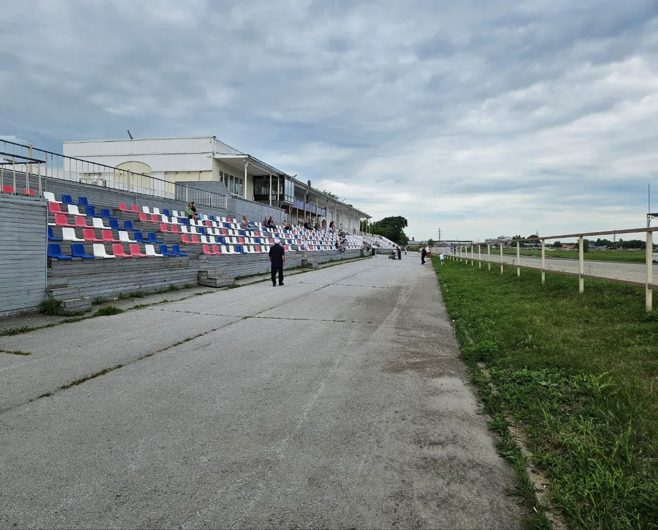 С другой стороны здания трибуны и сам ипподром. Людей не очень много.